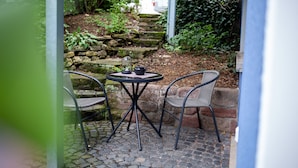 An outdoor patio with a round table and two chairs, surrounded by stone steps and greenery.