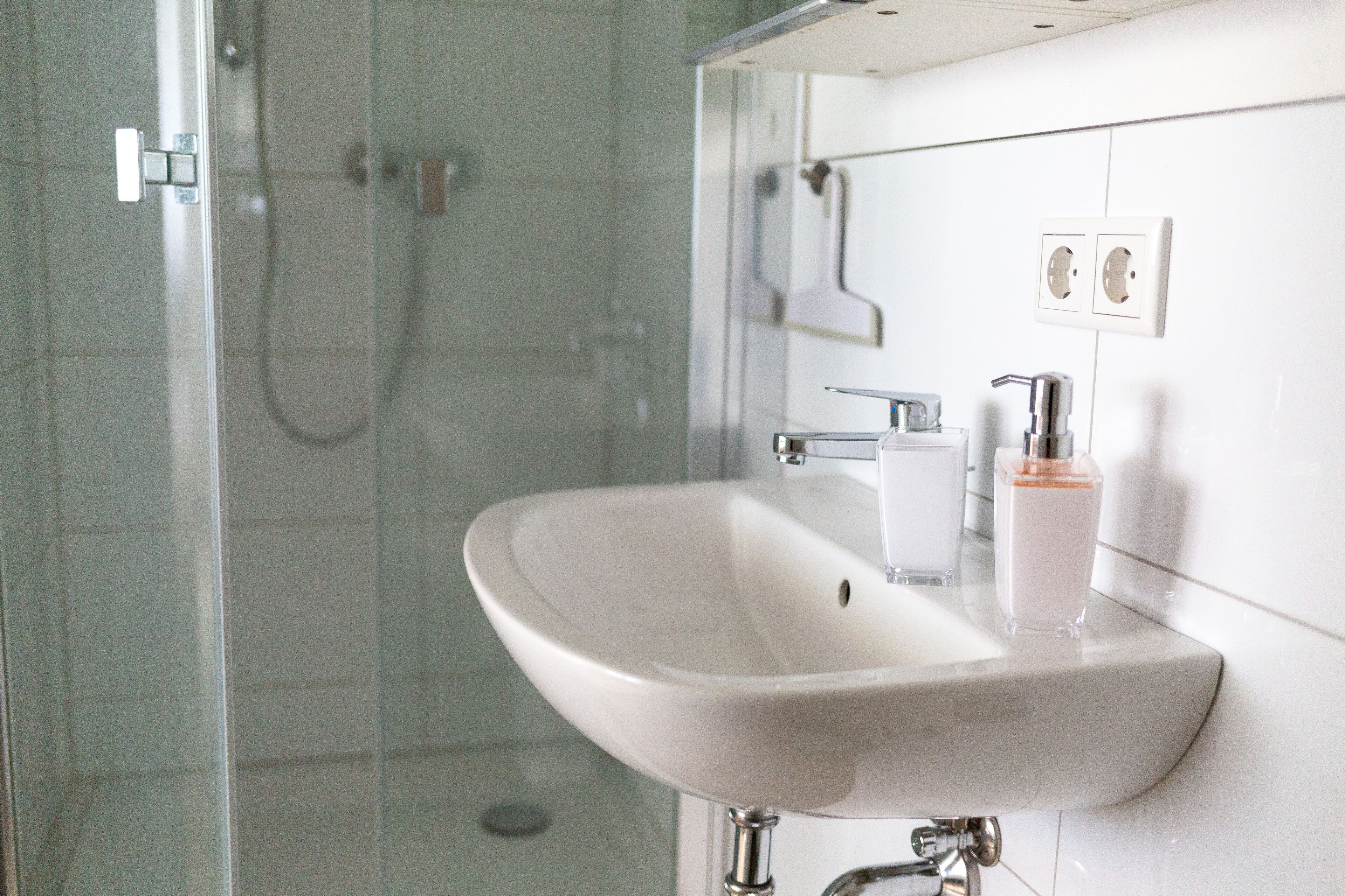 A bathroom with a glass shower enclosure, a white sink with a soap dispenser, and a mirror.