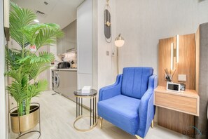 Ein modernes Wohnzimmer mit blauem Sessel, einem kleinen runden Tisch, einer Topfpflanze, einer Mikrowelle und einem Holzsideboard.