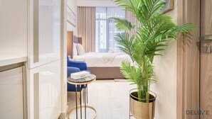 Moderni hotellihuone, jossa on sänky, sininen nojatuoli, pieni pöytä ja ruukussa oleva kasvi.