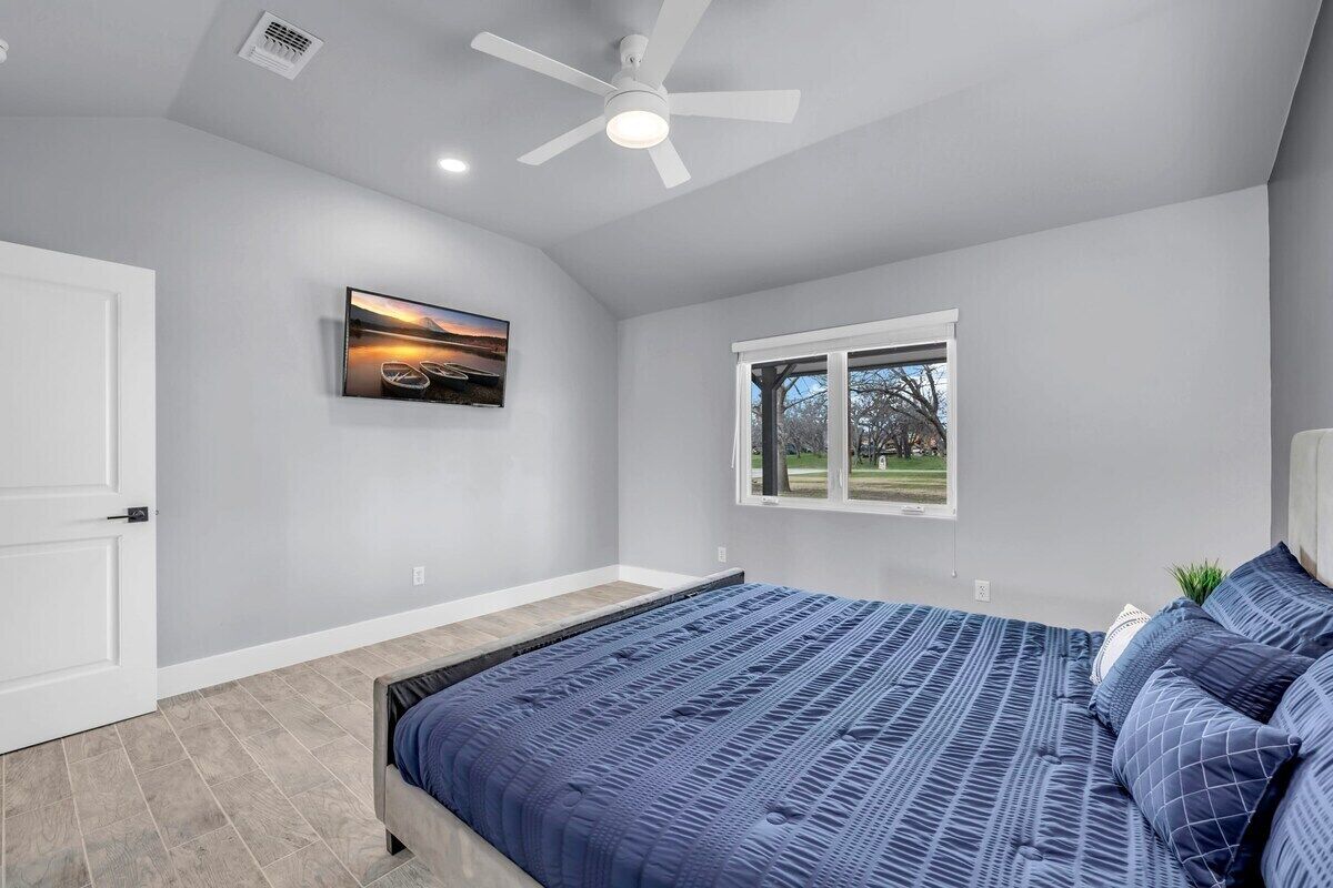 Una camera da letto con un letto, una ventola a soffitto, una finestra e un quadro appeso al muro.