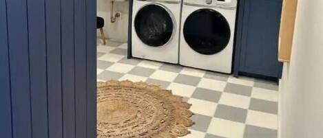 Un lavadero con dos lavadoras, un suelo a cuadros y una puerta azul.