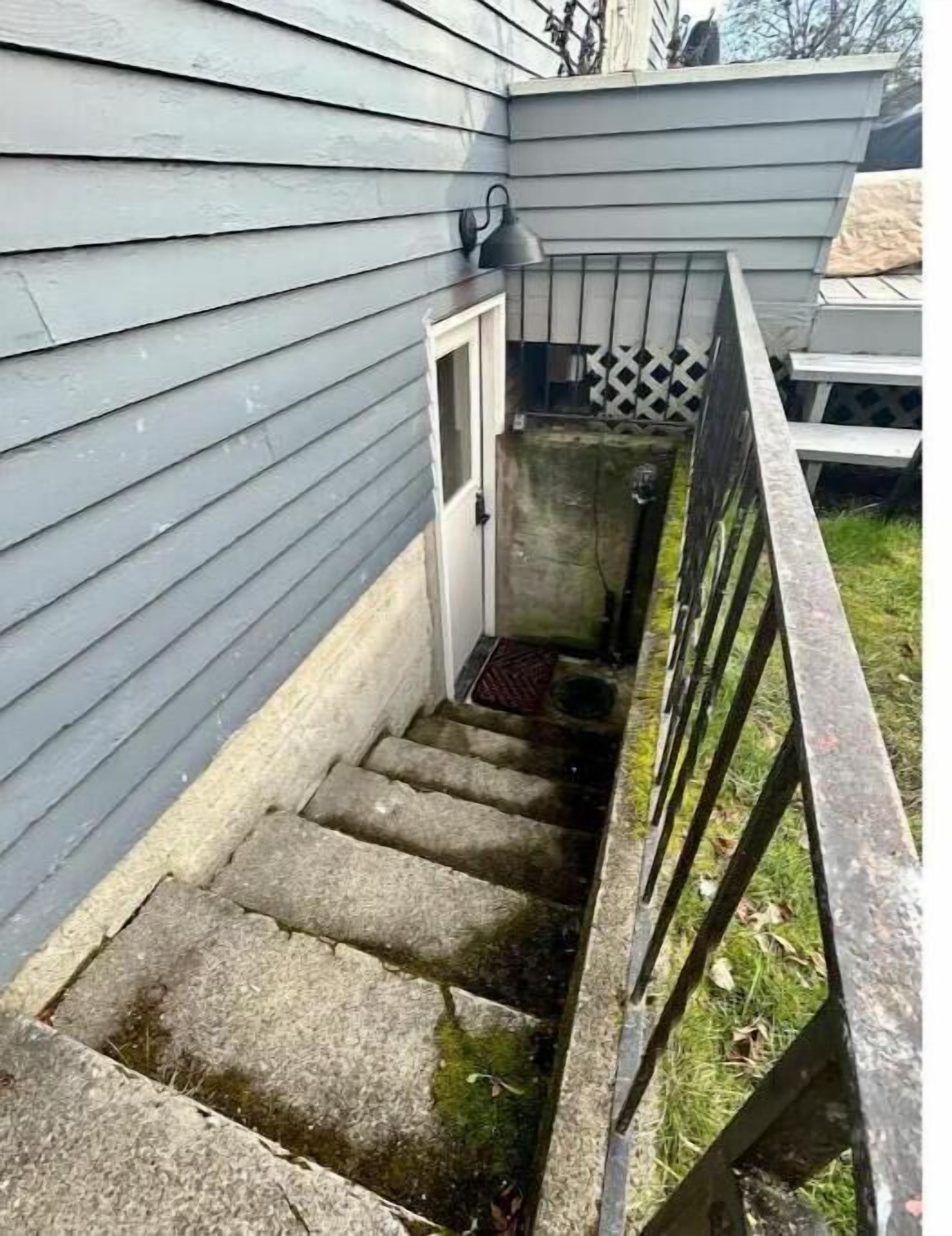 A narrow concrete staircase leading to a door, surrounded by a wooden fence and a small garden area.