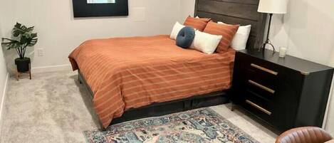 Un dormitorio con cama, mesita de noche, lámpara, planta en maceta y alfombra.