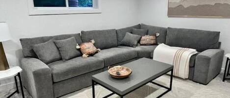A modern living room with a grey sectional sofa, a coffee table, and a patterned rug.