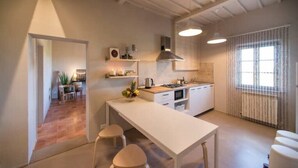 Cuina moderna amb armaris blancs, una illa central i il·luminació penjant.
