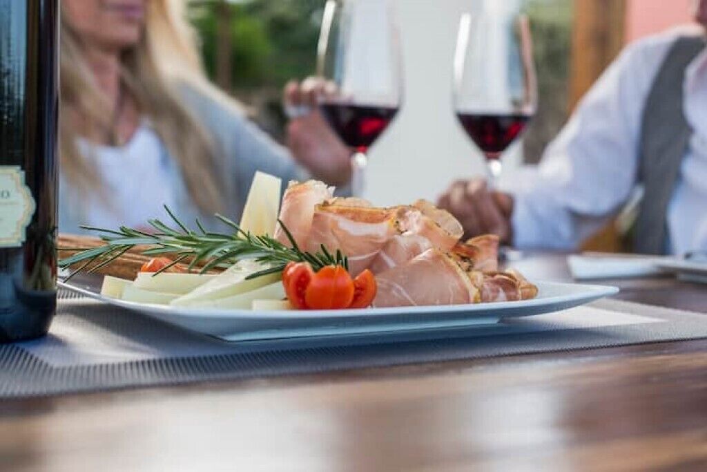 A dining table with a plate of food, a bottle, and two glasses of red wine.