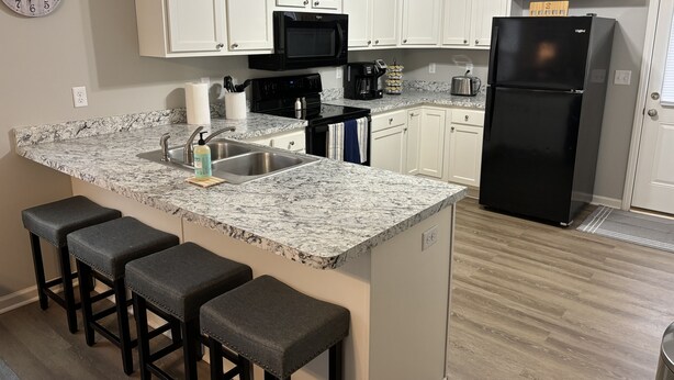 A modern kitchen with white cabinets, a black refrigerator, a microwave, and a granite countertop.