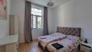 Een slaapkamer met een bed, nachtkastje, kledingkast en raam met gordijnen.