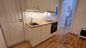 Een kleine keuken met witte kastjes, een houten aanrecht, een spoelbak en een vaatwasser.
