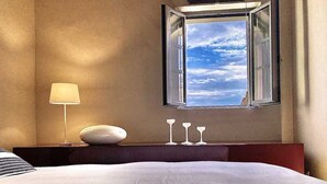 A hotel room with a large bed, a bedside lamp, a window with an open view, and three wine glasses on the windowsill. - Immersed in the silence of the Tuscan countryside, the Superior apartment offers an unspoiled view of the Tuscan countryside.Equipped with a kitchenette, living room, private bathroom and 2 bedrooms, 1 double bed and 1 queen bed, it offers: stove, refrig (Siena)