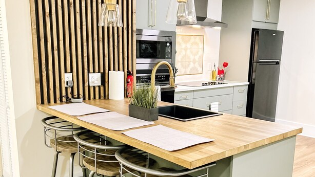 A modern kitchen with a central island, bar stools, a microwave, and a refrigerator.