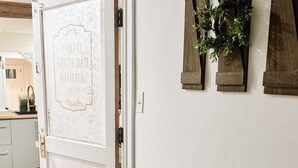 A white door with a decorative panel, a wooden floor, and a wall-mounted plant.