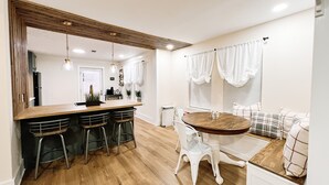 A modern kitchen with a wooden island, bar stools, and a dining table with white chairs.