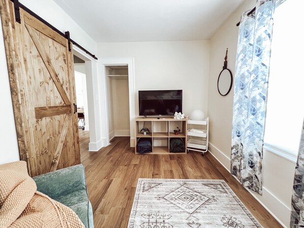 Una sala de estar con piso de madera, un televisor sobre un mueble de madera, una puerta corrediza y una alfombra estampada.