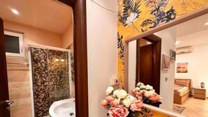 Une salle de bain avec une douche, un lavabo et un miroir, le tout décoré d’un papier peint à motifs floraux.