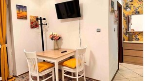 Un petit coin repas avec une table et deux chaises, un téléviseur à écran plat fixé au mur et un vase avec des fleurs sur la table.