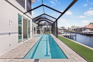 A pool area with a clear view of the water, a covered walkway, and a boat dock. - 2024 Monsterrat Model | Waterfront Home & Lap Pool (Marco Island)