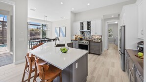 A modern kitchen with a large island, grey cabinets, and stainless steel appliances. - 2024 Monsterrat Model | Waterfront Home & Lap Pool (Marco Island)