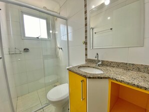 A bathroom with a shower, toilet, sink, and mirror. - Residencial Octávio Braga (Praia Grande)