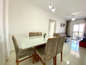 A dining area with a glass table, cushioned chairs, pendant lighting, and a view to a balcony. - Residencial Octávio Braga (Praia Grande)