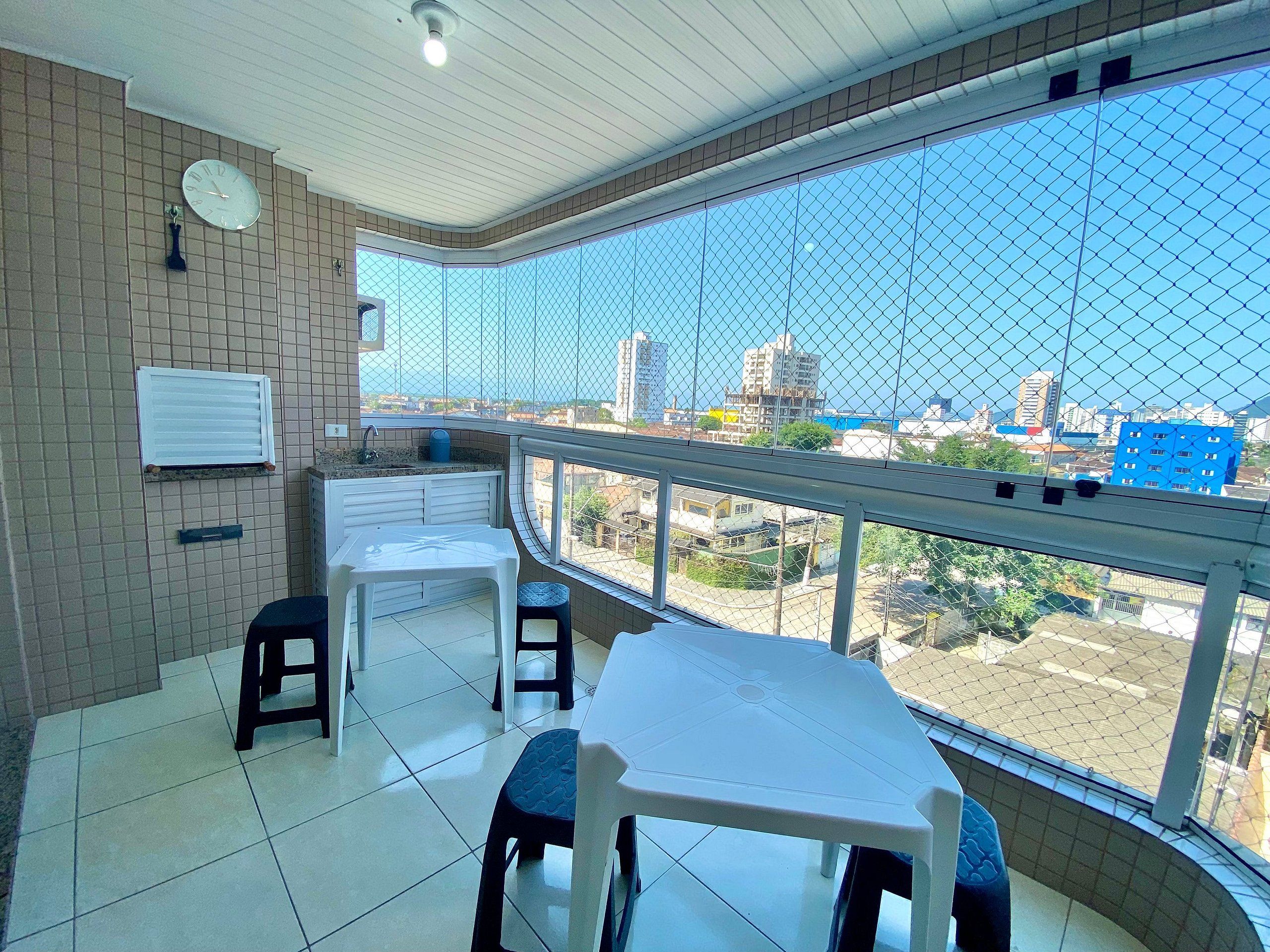 A balcony with a view of a cityscape, a white table, two chairs, a small sink, and a clock on the wall.