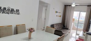 A modern living room with a sofa, a dining table with chairs, and a balcony with curtains. - Residencial Octávio Braga (Praia Grande)