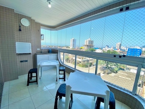 A balcony with a view of a cityscape, a white table, two chairs, a small sink, and a clock on the wall.