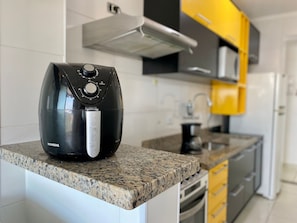 A kitchen with a black air fryer on a granite countertop, a stainless steel range hood, and yellow cabinets. - Residencial Octávio Braga (Praia Grande)