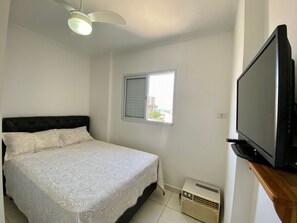 A bedroom with a bed, a ceiling fan, a window, and a television. - Residencial Octávio Braga (Praia Grande)