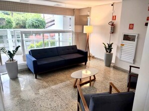 A modern hotel lobby with a blue sofa, a round table, and potted plants. - Residencial Octávio Braga (Praia Grande)