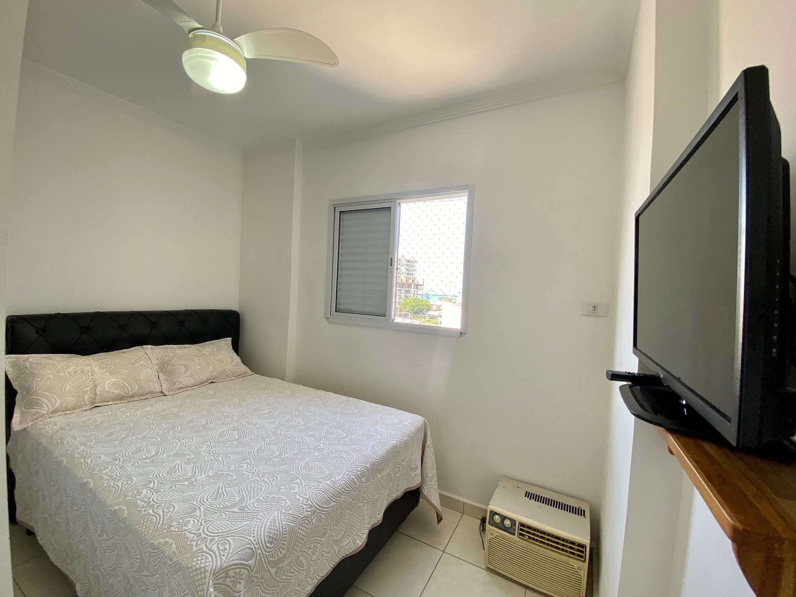 Un dormitorio con cama, ventilador de techo, ventana y televisor.