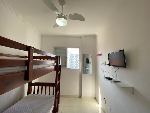 A room with a bunk bed, a ceiling fan, a television mounted on the wall, and a window with blinds.
