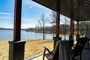Un espacio exterior cubierto con vistas a un lago, sillas de madera y un pilar de ladrillo.