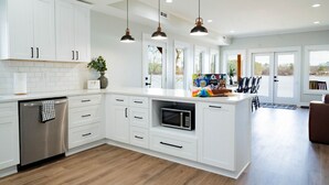 Una cocina moderna con armarios blancos, microondas integrado e iluminación colgante.