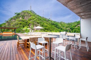 A deck with outdoor seating, a pool, and a view of a lush hill.