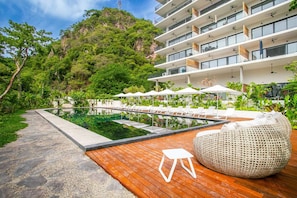 A modern hotel with a pool, outdoor seating, and lush greenery. - Two Pools, Bar & Gym | Casa Medianoche at Oasis (Puerto Vallarta)