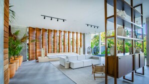 A modern living room with a sectional sofa, wooden slats, and a large window overlooking greenery. - Two Pools, Bar & Gym | Casa Medianoche at Oasis (Puerto Vallarta)