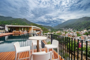 A terrace with a pool, dining area, and a view of a town and mountains. - Two Pools, Bar & Gym | Casa Medianoche at Oasis (Puerto Vallarta)