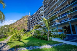 A multi-story hotel with balconies, a garden area with tropical plants, and a clear sky.