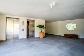 A spacious lobby with a large potted plant, a bench, and a wall-mounted circular mirror.