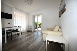 A modern living room with a sofa, a dining table with chairs, a TV mounted on the wall, and a sliding glass door leading to an outdoor area. - MODERN APARTMENT GROUND FLOOR AND PARKING SPACE APP WATER (Malcesine)