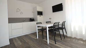 A modern kitchen with white cabinets, a white dining table with four chairs, a flat-screen TV mounted on the wall, and a coffee maker on the counter.