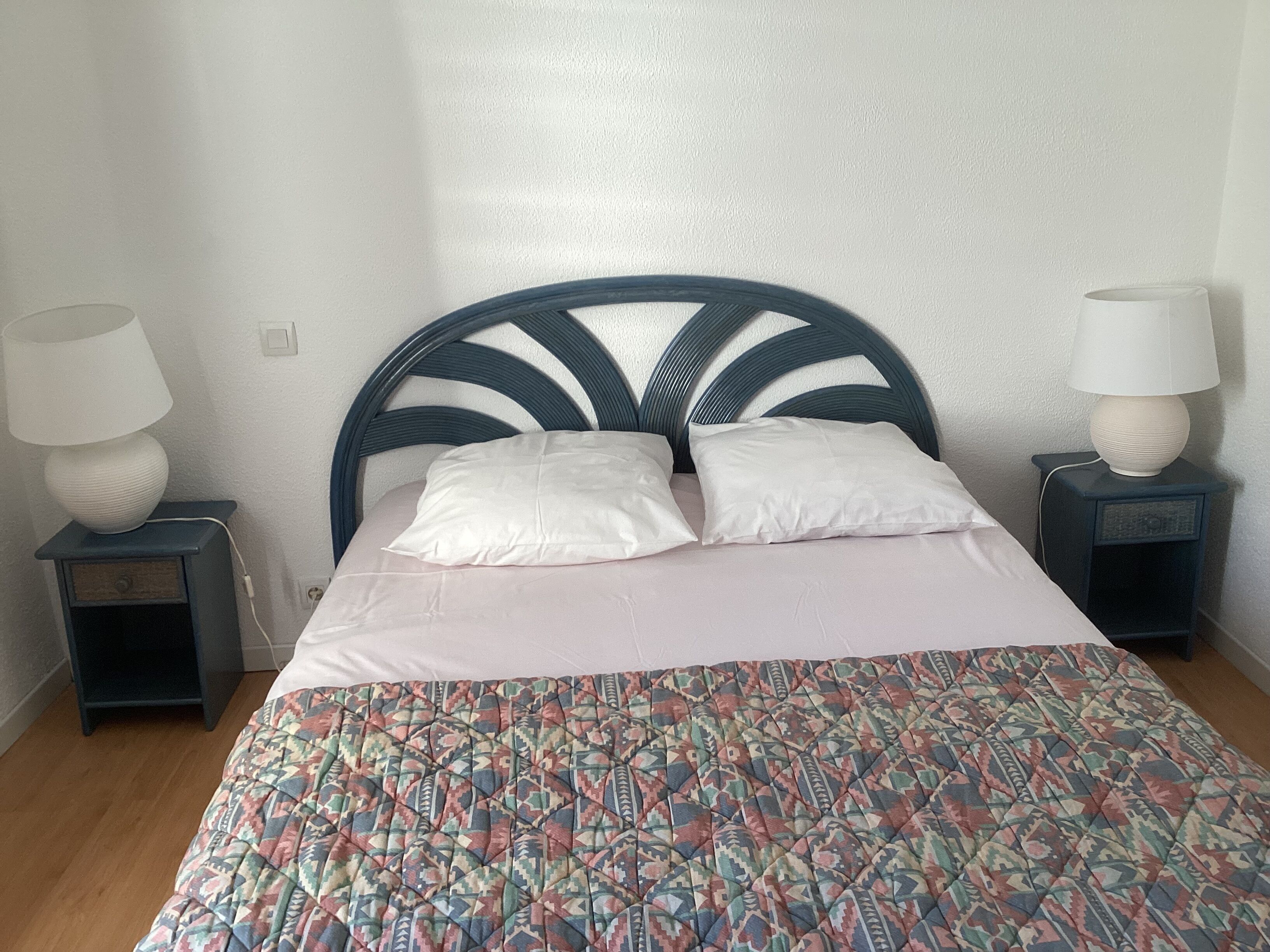 A neatly made bed with a patterned bedspread, two bedside lamps, and a dark headboard.