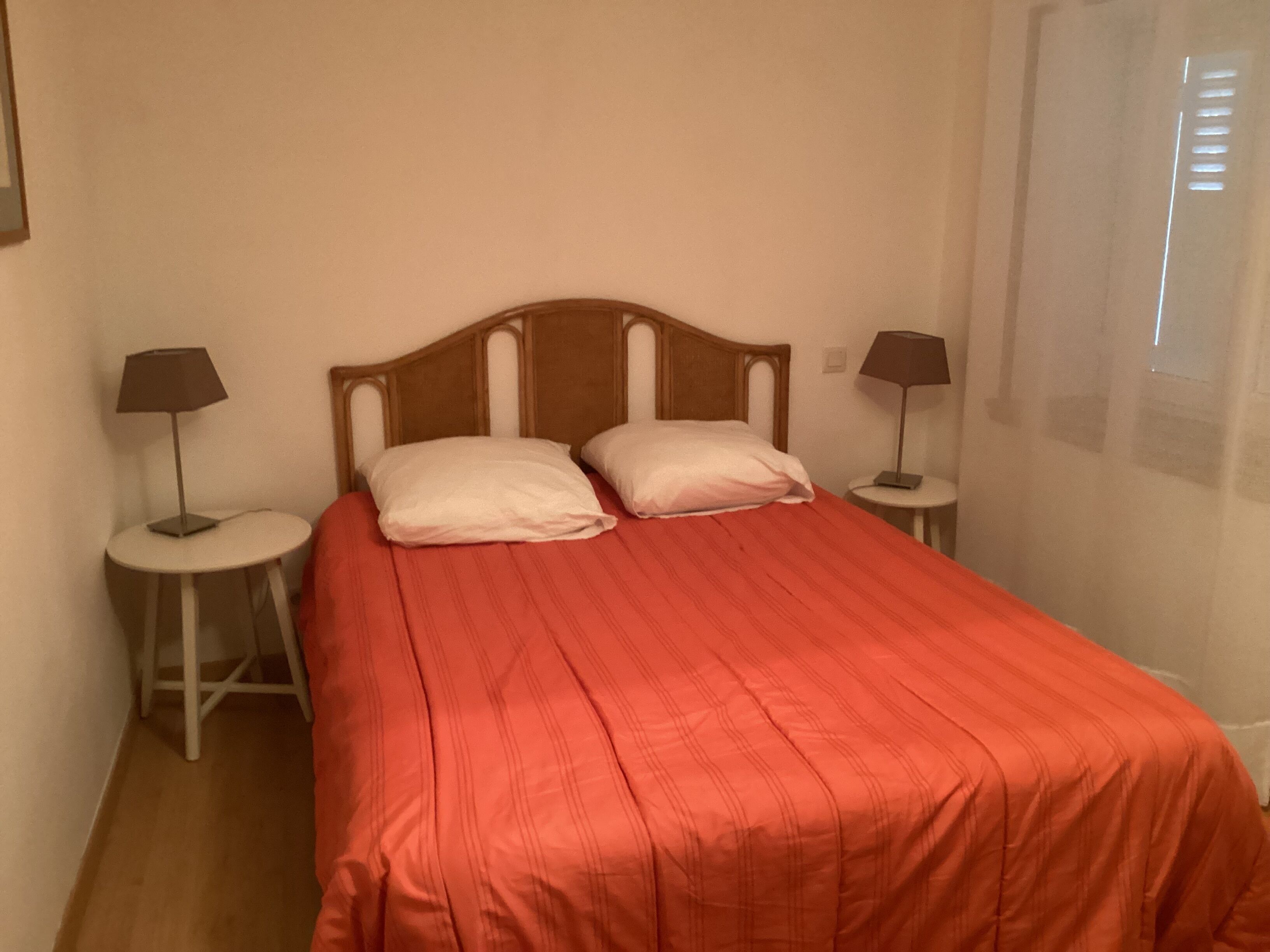 Een kamer met een enkel bed, twee nachtkastjes en een raam met jaloezieën.