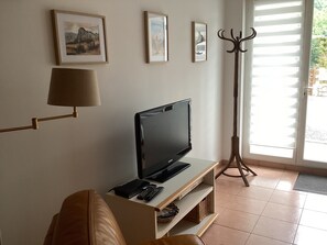 Una sala de estar con televisor, lámpara y perchero.