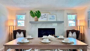 A dining area with a wooden table set for four, flanked by two chairs, a fireplace, and framed artwork above. - Private Pool + 2 King Beds | 8 Min to IRB (Largo)