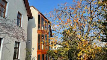 A two-story building with a balcony, a garden with a bench, and a tree with autumn leaves.