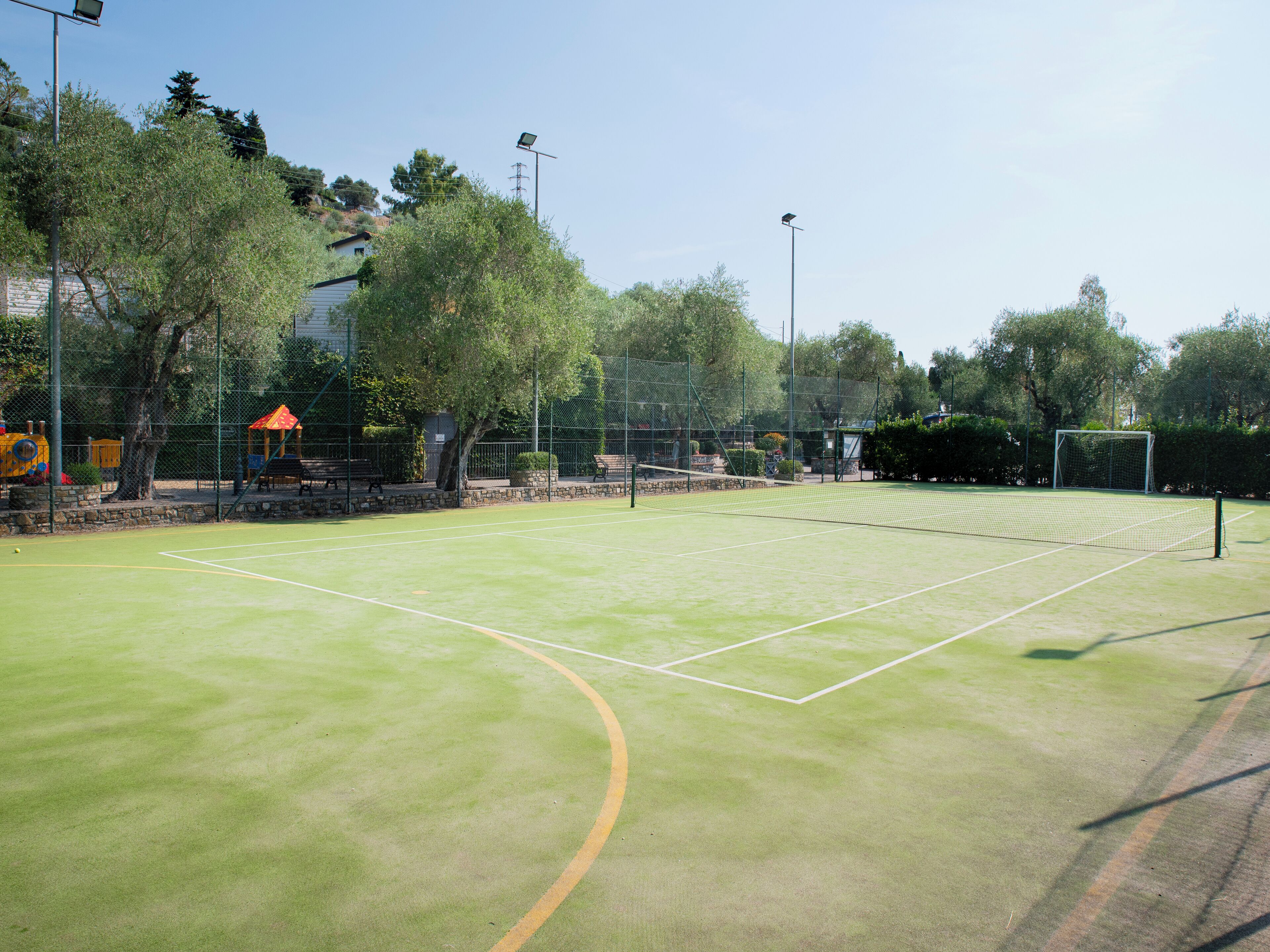 Una cancha de tenis con red, rodeada de árboles y una valla.
