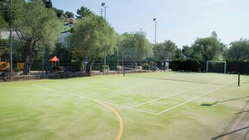 Una cancha de tenis con red, rodeada de árboles y una valla.